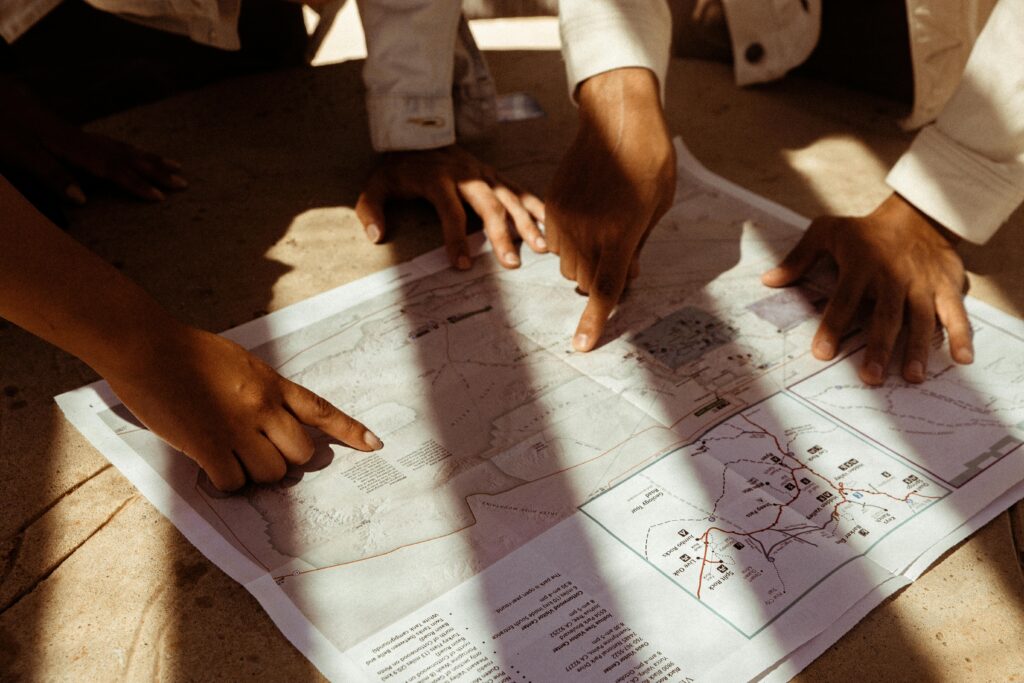 pexels photo 2981107 2981107 Group of hands pointing at a detailed map, planning an adventure trip in sunlight.