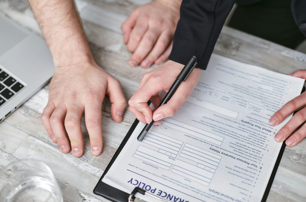 pexels photo 7734574 7734574 Close-up image of two people signing an insurance policy document on a wooden desk.