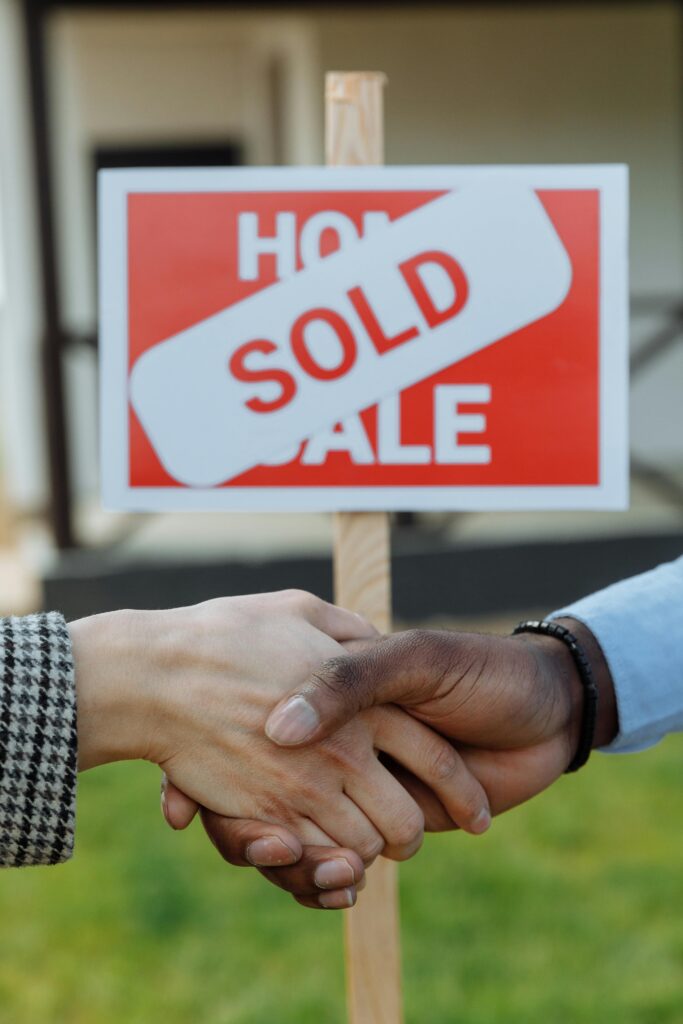 pexels photo 8470811 8470811 Close-up of a handshake in front of a sold sign symbolizing a successful real estate transaction.