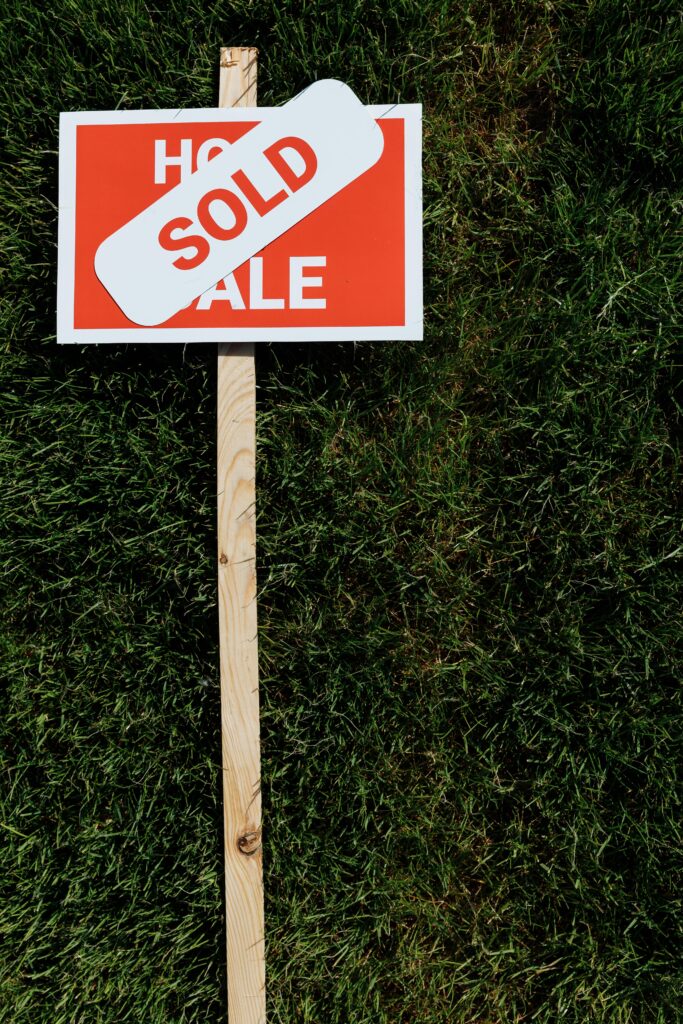 pexels photo 8470834 8470834 Red 'Sold' sign on wooden post stands on green grass lawn, symbolizing property sale.